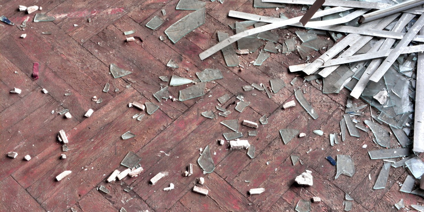 Broken glass and torn window blinds scattered across wood floor.